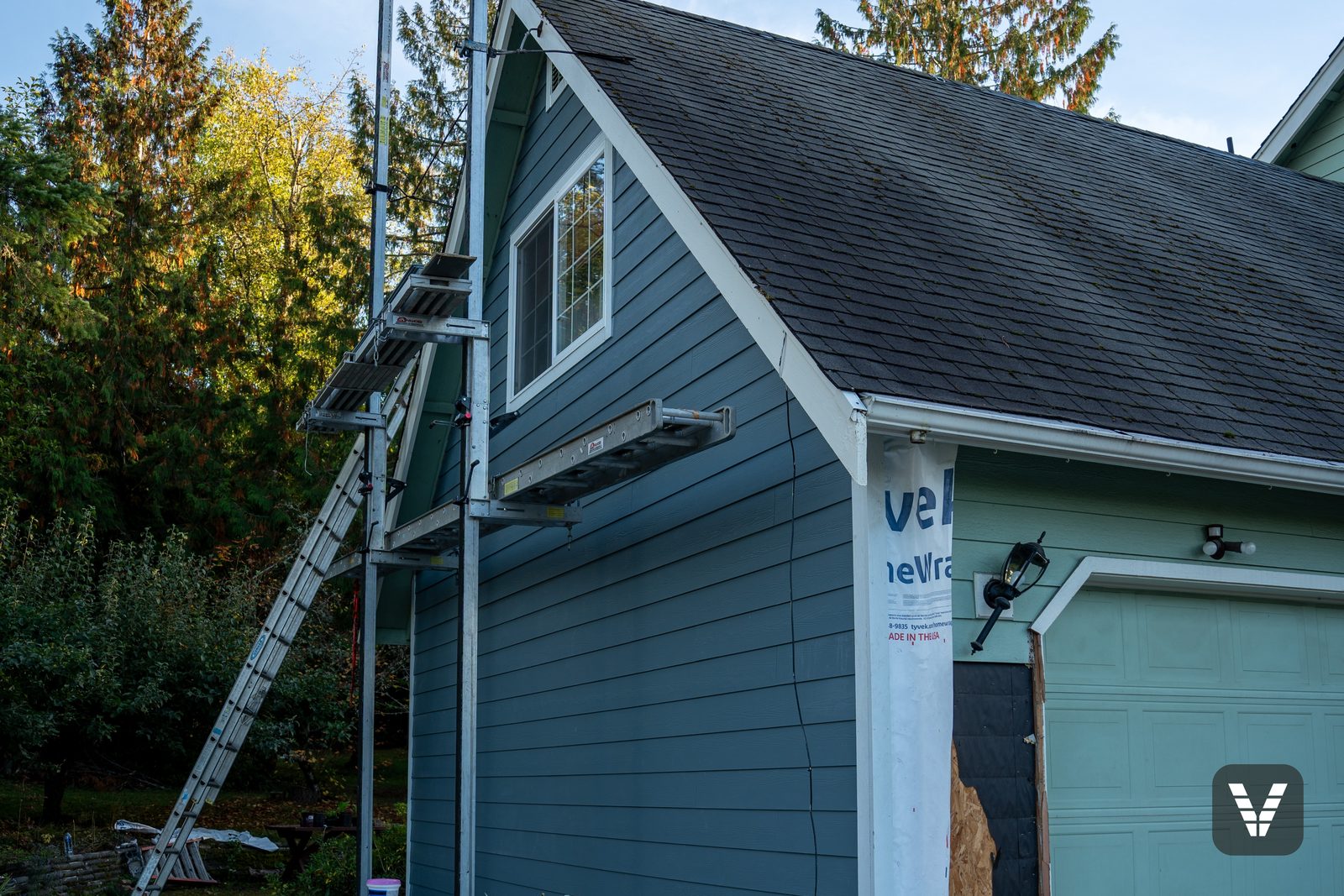 Mid-install — HomeWrap on the garage wall, scaffolding up, the first Boothbay Blue planks running