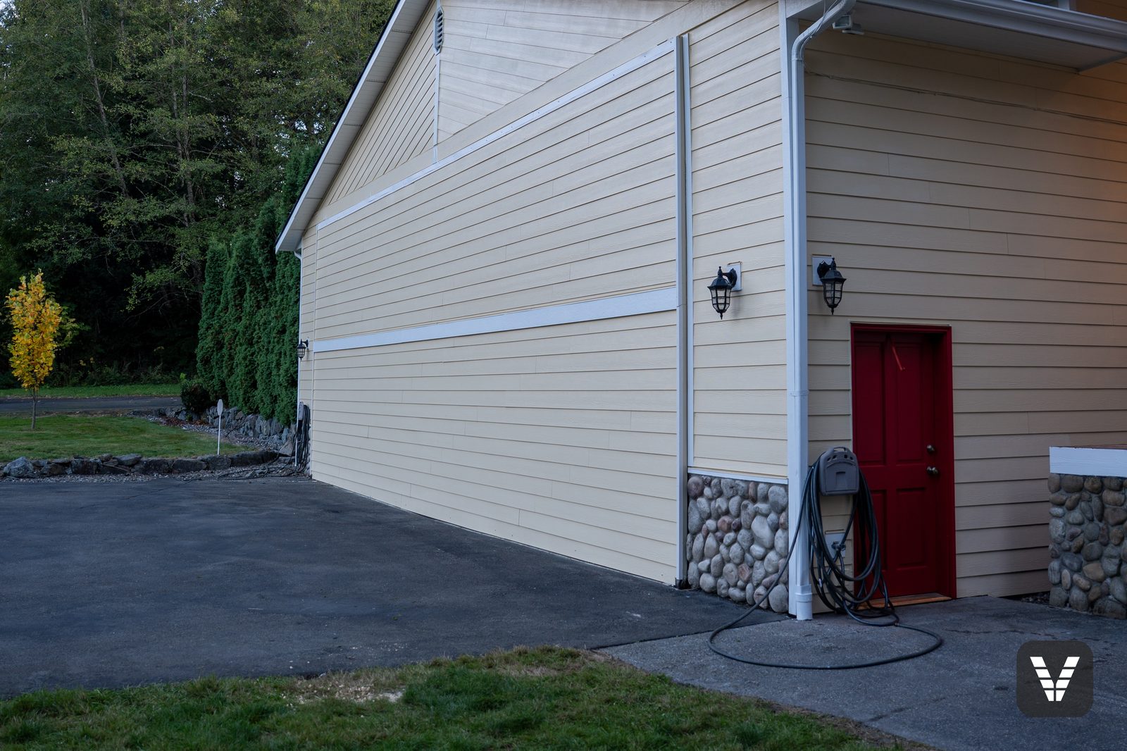 Hangar side door in red against fresh lap siding and rock skirt — Siding & Window Vault project in Lake Stevens, WA